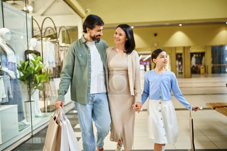 Téléchargez les photos : Une famille heureuse, tenant des sacs à provisions, se promenant dans un centre commercial animé lors d'une sortie de week-end amusante. - en image libre de droit