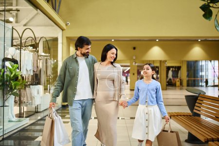Una familia feliz, llevando bolsas de la compra, camina a través de un centro comercial bullicioso en una excursión de fin de semana juntos.