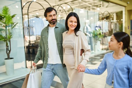 Eine schwangere Frau und ihre Tochter spazieren fröhlich zusammen in einem belebten Einkaufszentrum auf einem lustigen Familienausflug.