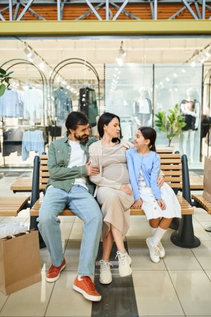 Eine glückliche Familie sitzt auf einer Bank in einem belebten Einkaufszentrum und genießt einen entspannten Moment zusammen während ihres Wochenendausflugs.