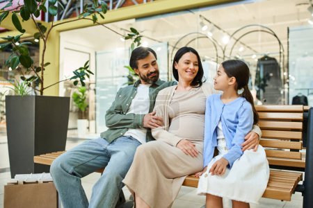 Téléchargez les photos : Une famille joyeuse profite d'une journée shopping, assise ensemble sur un banc dans un centre commercial animé. - en image libre de droit