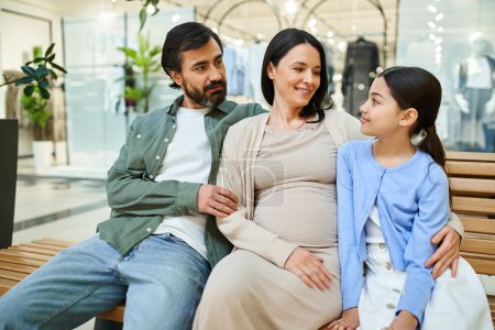 Téléchargez les photos : Une femme enceinte et sa fille s'assoient sur un banc, profitant d'un week-end shopping au centre commercial ensemble. - en image libre de droit