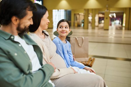Photo for A content family enjoys a break on a bench in a bustling shopping mall during a fun weekend outing. - Royalty Free Image