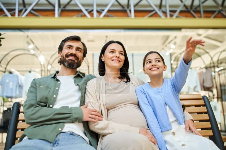 Téléchargez les photos : Une famille joyeuse avec des enfants assis ensemble sur un banc dans un centre commercial occupé, prenant une pause de shopping. - en image libre de droit