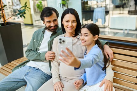 Eine quirlige Familie genießt ein Shopping-Wochenende, sitzt auf einer Bank in einem Einkaufszentrum und macht gemeinsam ein fröhliches Selfie.