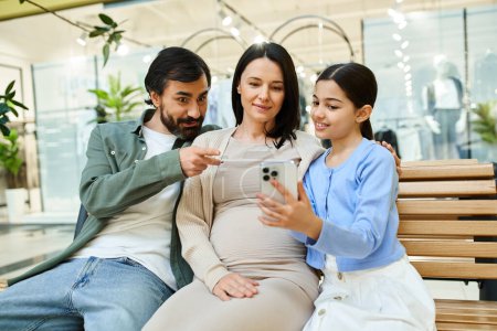 Téléchargez les photos : Une famille est assise sur un banc dans un centre commercial, engloutie dans un écran de téléphone portable ensemble. - en image libre de droit