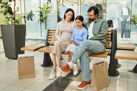 Eine fröhliche Familie entspannt sich während eines Wochenendausflugs auf einer Bank in einem belebten Einkaufszentrum.