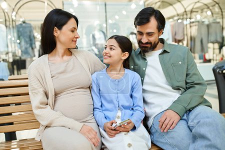 Eine schwangere Frau und ihre Tochter verbringen einen zärtlichen Moment auf einer Bank in einem belebten Einkaufszentrum.