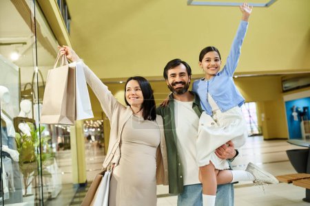 Eine glückliche Familie wird gesehen, wie sie Einkaufstüten hält, während sie gemeinsam das Einkaufszentrum auf einem lustigen Wochenendausflug erkundet.