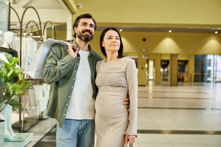 A pregnant woman and man happily walk together in a bustling shopping mall on a weekend outing.