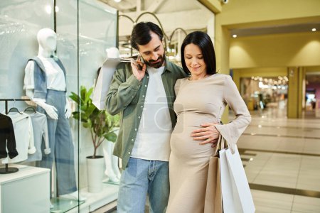 A pregnant man and woman happily walk through a bustling shopping mall on a weekend outing.