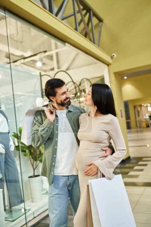 Una alegre pareja embarazada caminando en un centro comercial, sosteniendo bolsas llenas de golosinas, disfrutando de un fin de semana juntos.