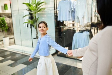 A woman and a young girl happily shop for clothes together in a bustling store.
