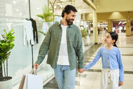 Foto de A man and a girl happily walk through a mall, holding shopping bags filled with purchases. - Imagen libre de derechos