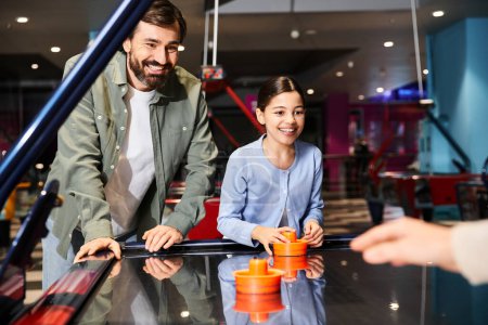 Vater und Tochter spielen in einer Spielzone in einem Einkaufszentrum ein freundschaftliches Airhockey, was eine lebendige und lustige Atmosphäre schafft