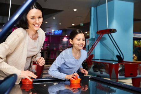 A happy mother and child play air hockey in a mall gaming zone during a weekend outing, enjoying quality time together.