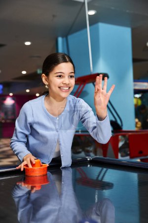 A girl joyfully competes in a game of air hockey with family at a mall gaming zone during the weekend.