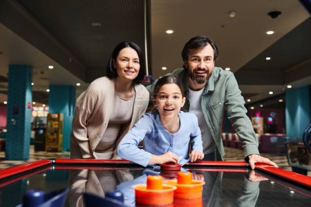 A happy family competes in a game of air hockey at an arcade, laughing and enjoying a fun weekend together.