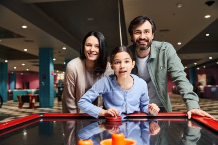 Una familia alegre jugando hockey aéreo con entusiasmo en una animada zona de juegos de los centros comerciales en un animado fin de semana.