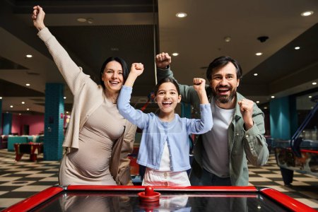 Une famille joyeuse concourt dans un jeu animé de hockey aérien dans une arcade, entouré de lumières clignotantes et le son du rire.