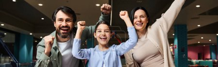 Foto de A delighted family raises their arms in a malls gaming zone, celebrating unity and happiness during a weekend outing. - Imagen libre de derechos