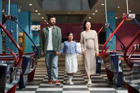 A happy family is joyfully walking through a air hockey in a mall during the weekend, enjoying a day of fun together.