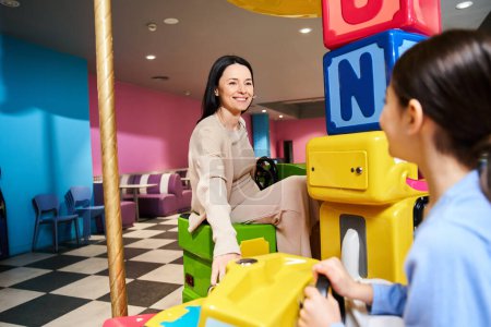 Foto de Una mujer juega alegremente con un niño en una sala de juguetes vibrante, rodeada de juguetes y juegos coloridos. - Imagen libre de derechos