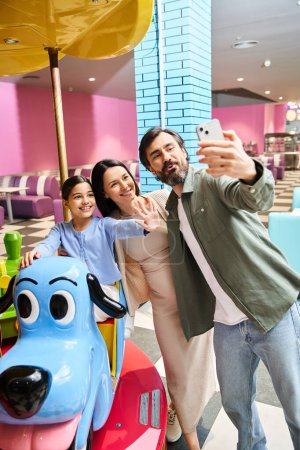 Eine glückliche Familie genießt einen Selfie-Moment, während sie am Wochenende von einem Spielzeugkarussell in einem Einkaufszentrum umgeben ist.