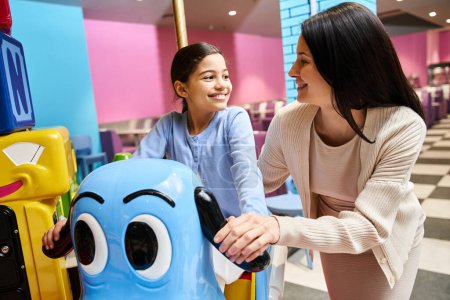 Eine Frau und ein Kind lachen, als sie am Wochenende in einem lebhaften Spielwarengeschäft in einem belebten Einkaufszentrum mit einem Spielzeugkarussell spielen.