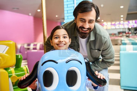 A man and child happily pose next to a toy car in a gaming zone of a mall during the weekend.