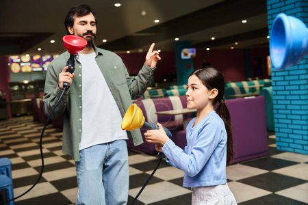 A father and his daughter happily play a game in a gaming zone within a mall on a weekend.