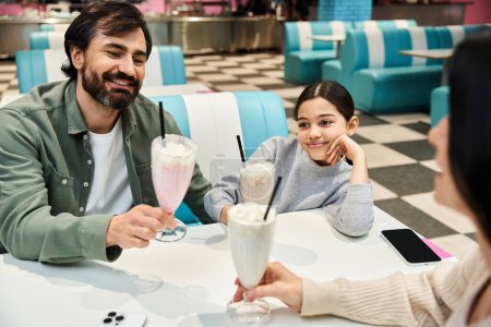 Téléchargez les photos : Une famille heureuse aime les milkshakes lors d'un dîner pendant le week-end, riant et partageant du bon temps ensemble. - en image libre de droit