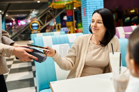 Téléchargez les photos : Une femme remet une carte de crédit à une serveuse dans un restaurant, incarnant des liens familiaux modernes pendant le week-end. - en image libre de droit