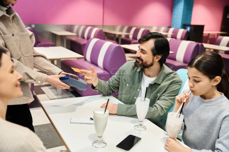 Foto de Una familia feliz se sienta en una mesa de restaurante, el hombre entrega una tarjeta de crédito a una camarera - Imagen libre de derechos