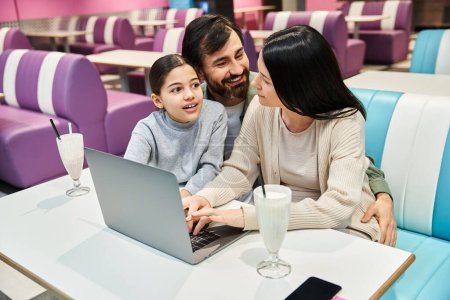 Una familia alegre disfruta del tiempo de calidad juntos en un restaurante mientras se reúnen alrededor de una computadora portátil.