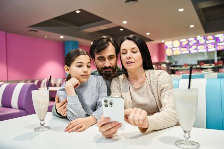 Photo for A happy family is gathered around a table, absorbed in a cell phone, spending quality time together in a modern setting. - Royalty Free Image