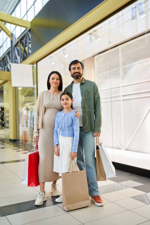 A happy family stands in a shopping mall, each holding multiple shopping bags filled with purchases from their weekend spree.
