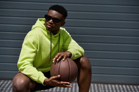 Joven afroamericano con capucha verde sosteniendo una pelota de baloncesto.