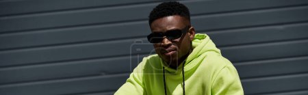 A fashionable African American man wearing a green hoodie and sunglasses.
