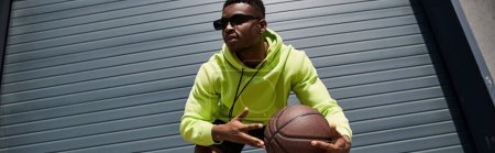 Foto de Hombre afroamericano con capucha verde sosteniendo baloncesto. - Imagen libre de derechos