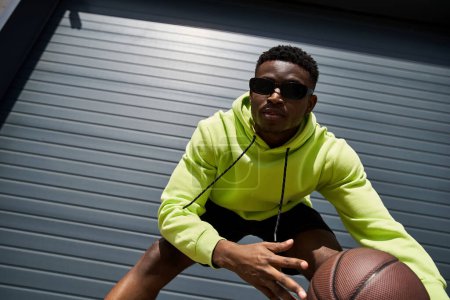 African American man in green hoodie holds basketball.