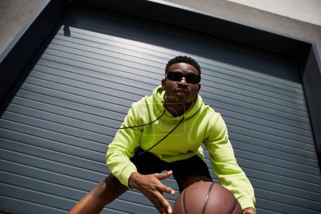Hombre afroamericano guapo con capucha verde sosteniendo baloncesto.