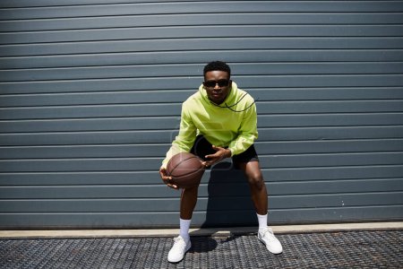 Photo for A trendy young man in a green hoodie holds a basketball. - Royalty Free Image