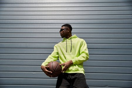 Foto de Elegante, hombre afroamericano con capucha de neón que sostiene el baloncesto. - Imagen libre de derechos