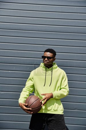 Junger Afroamerikaner in neongrünem Kapuzenpulli hält Basketball in der Hand.