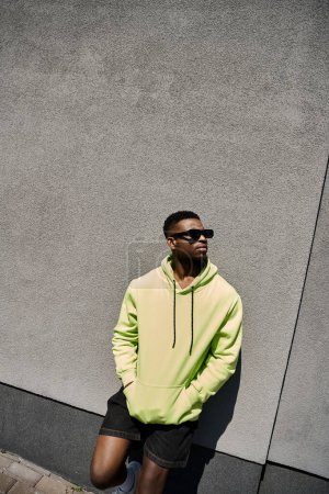 Photo for Handsome African American man in a yellow hoodie leans against a wall. - Royalty Free Image