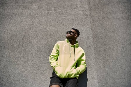Stylish African American man in a yellow hoodie leaning against a wall.