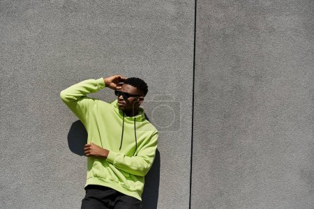 Stylish young man in neon hoodie leaning against wall.