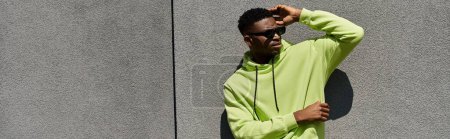 Handsome African American man leaning against wall in stylish green hoodie.