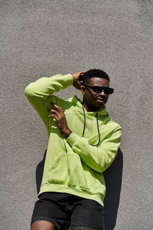 Handsome African American man in lime green hoodie leaning against wall.